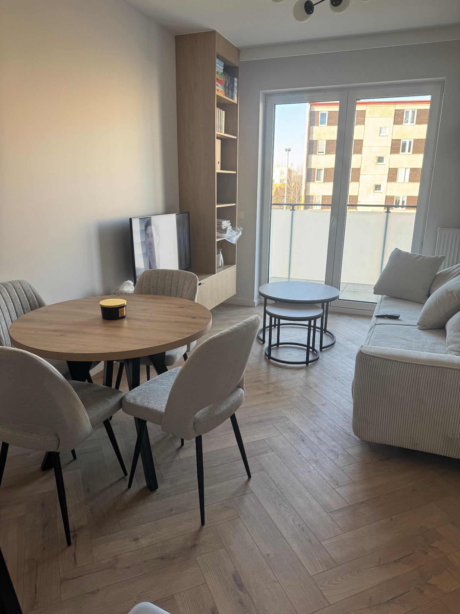 Jasne wnętrze po remoncie w Tomaszowie Mazowieckim: parkiet w jodełkę, okrągły stół z krzesłami, sofa i regał. Nowoczesny design, naturalne światło.