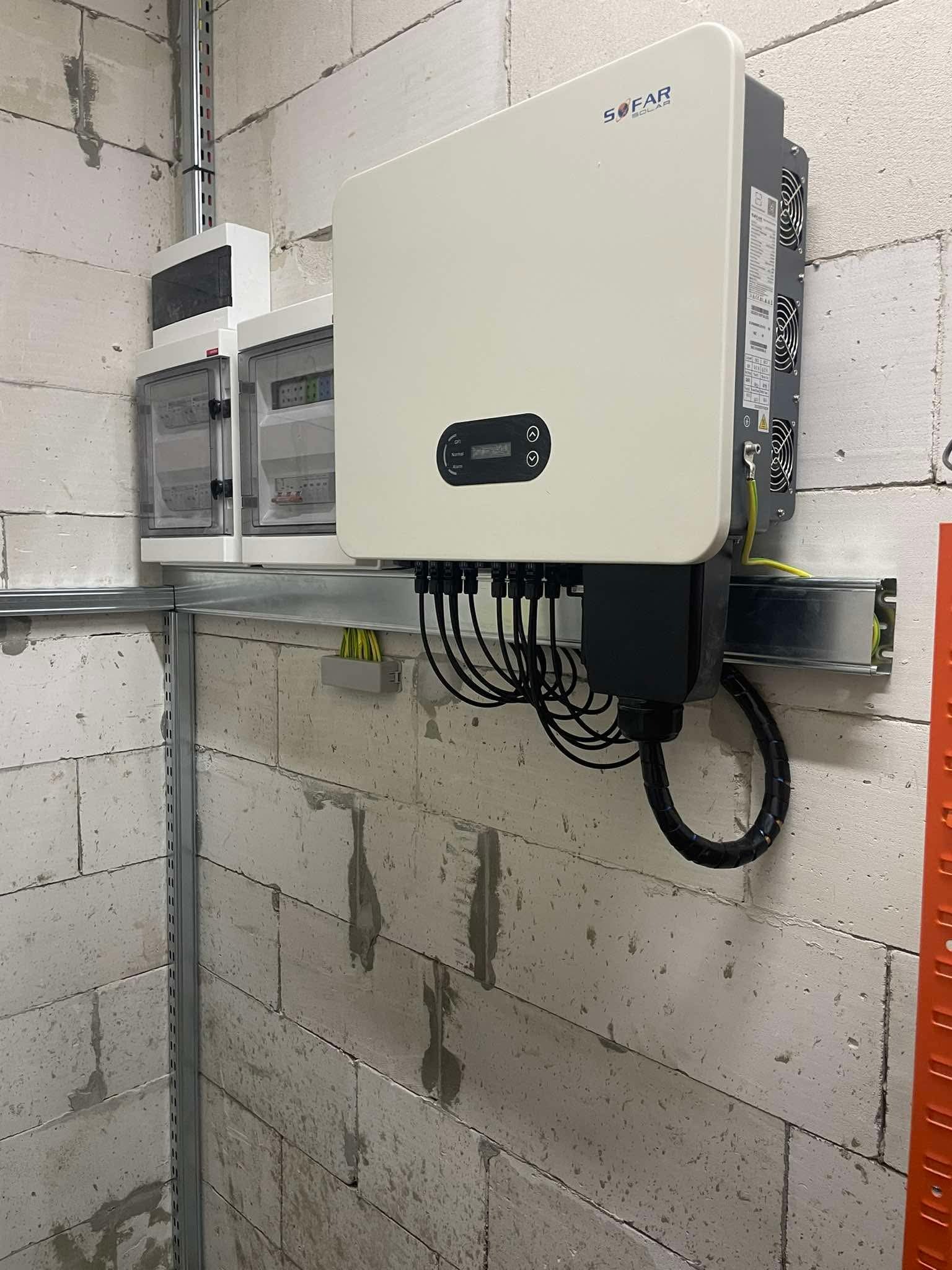 Biały inwerter Sofar Solar zamontowany na ścianie z bloczków, widoczne kable i zabezpieczenia, szyna montażowa. Instalacja w surowym pomieszczeniu.