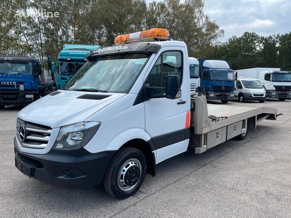 Biała laweta Mercedes Sprinter z pomarańczowym światłem ostrzegawczym na dachu, zaparkowana wśród innych pojazdów transportowych. Widok z przodu, lekki skos.