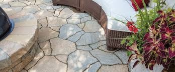 Nieregularna kamienna nawierzchnia patio z paleniskiem i meblami ogrodowymi. Jasne, naturalne światło podkreśla teksturę kamienia.