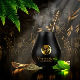 Eleganckie ujęcie czarnego matero Yerbador z złotą bombillą i suszem, na tle florystycznego wzoru. Liść i paproć dodają świeżości kompozycji.