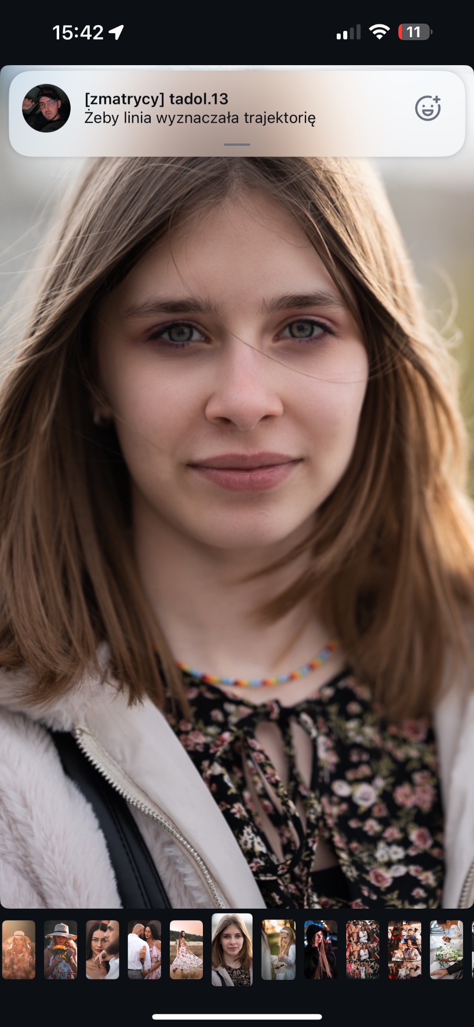 Portret młodej kobiety z kolorowym naszyjnikiem, w rozpiętej kurtce, z powiewającymi włosami, w naturalnym oświetleniu.