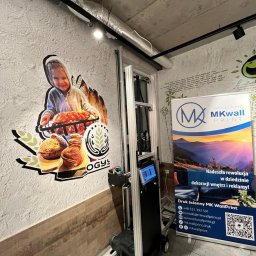 BaseElektric Artur Idasiak - Drukarka ścienna MK WallPrint w trakcie pracy, nanosi kolorową grafikę z motywem piekarniczym na ścianę o chropowatej fakturze w lokalu gastronomicznym.