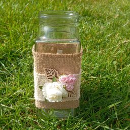 Kreator Uśmiechu - Szklany wazon zdobiony jutą i kwiatami, leżący na trawie. Dekoracja w stylu rustykalnym, idealna na przyjęcia okolicznościowe na świeżym powietrzu.
