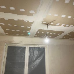 Kreator Budowlany Justyna Sawicka - Przygotowanie sufitu i ścian do malowania: szpachlowanie łączeń płyt gipsowo-kartonowych, zabezpieczone okno folią malarską, surowa żarówka.