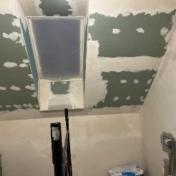 Kreator Budowlany Justyna Sawicka - Poddasze w trakcie szpachlowania: sufit ze świetlikiem, częściowo pokryty zieloną masą szpachlową, widoczne narzędzia i worki z materiałami.