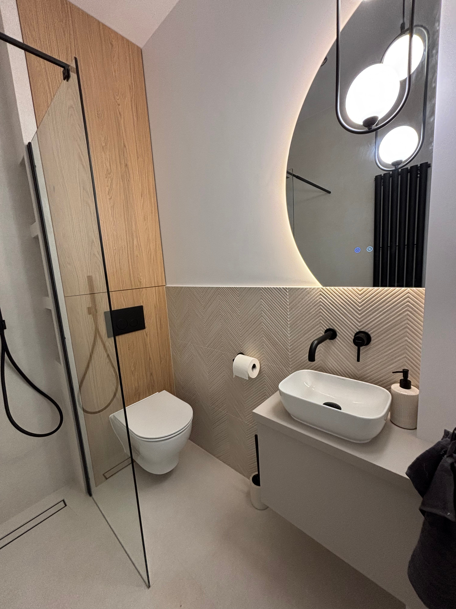 Nowoczesna łazienka z kabiną prysznicową typu walk-in, wiszącą toaletą i umywalką nablatową. Uwagę przyciąga duże, podświetlane lustro i armatura w kolorze czarnym.