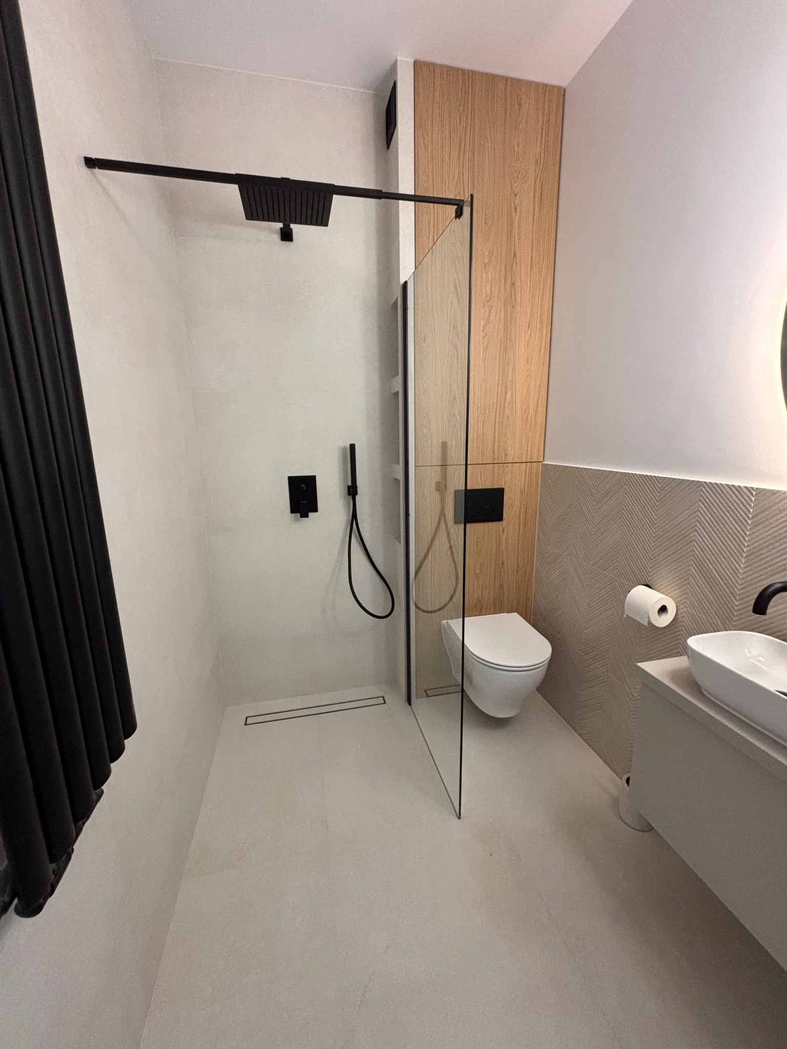 Nowoczesna łazienka z kabiną typu walk-in, drewnianą ścianą i umywalką nablatową. Czarna armatura dodaje elegancji. Minimalistyczny design.