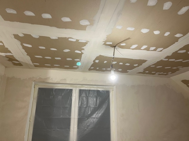 Przygotowanie sufitu i ścian do malowania: szpachlowanie łączeń płyt gipsowo-kartonowych, zabezpieczone okno folią malarską, surowa żarówka.