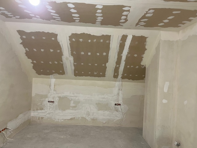 Pokój w trakcie szpachlowania: sufit z płyt gipsowych, ściany z widocznymi przewodami elektrycznymi. Widoczny etap prac przygotowawczych do malowania.