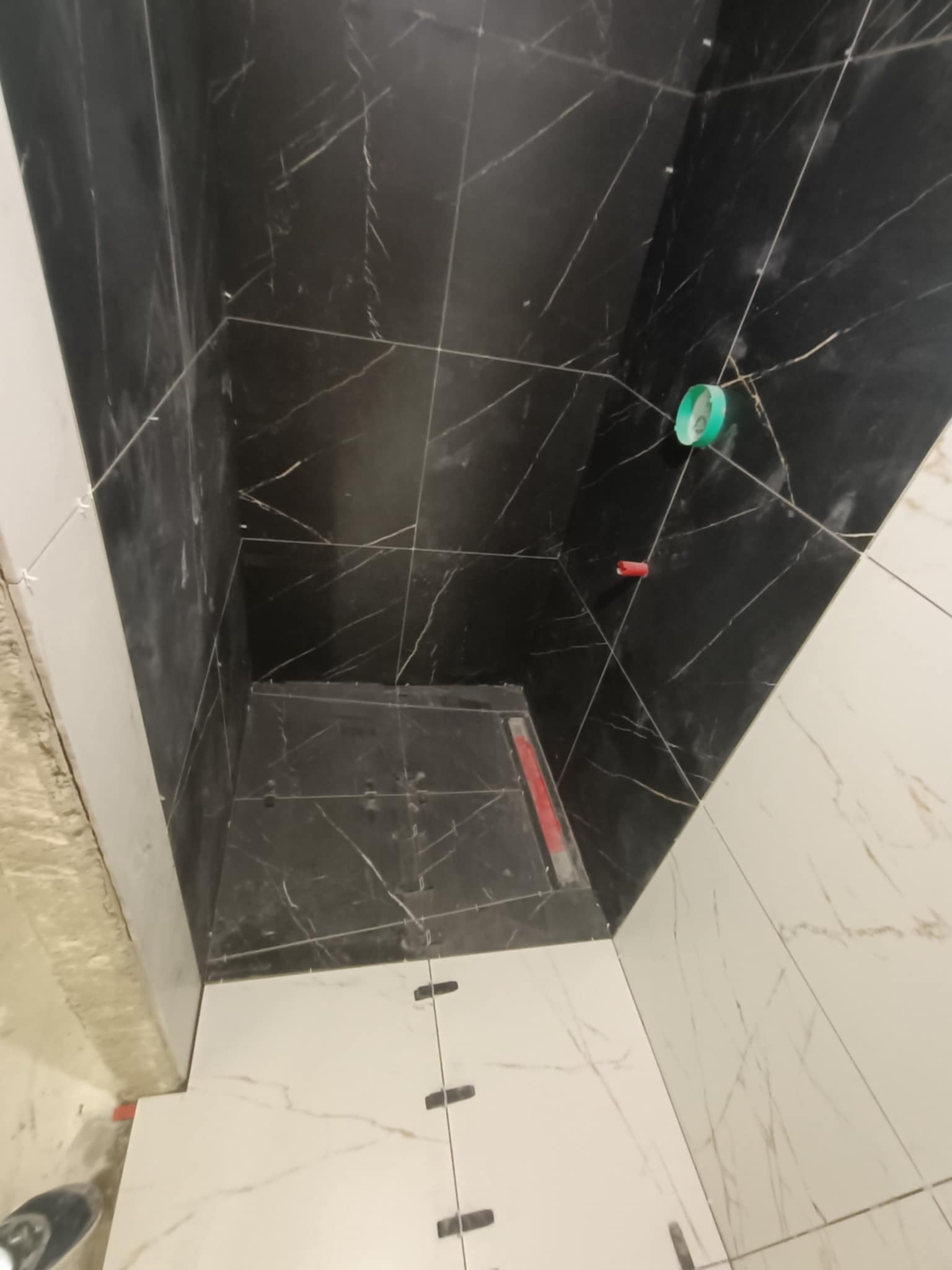 Czarno-biała glazura imitująca marmur w kabinie prysznicowej w trakcie montażu. Widoczne krzyżyki dystansowe i odpływ liniowy. Ujęcie z góry.