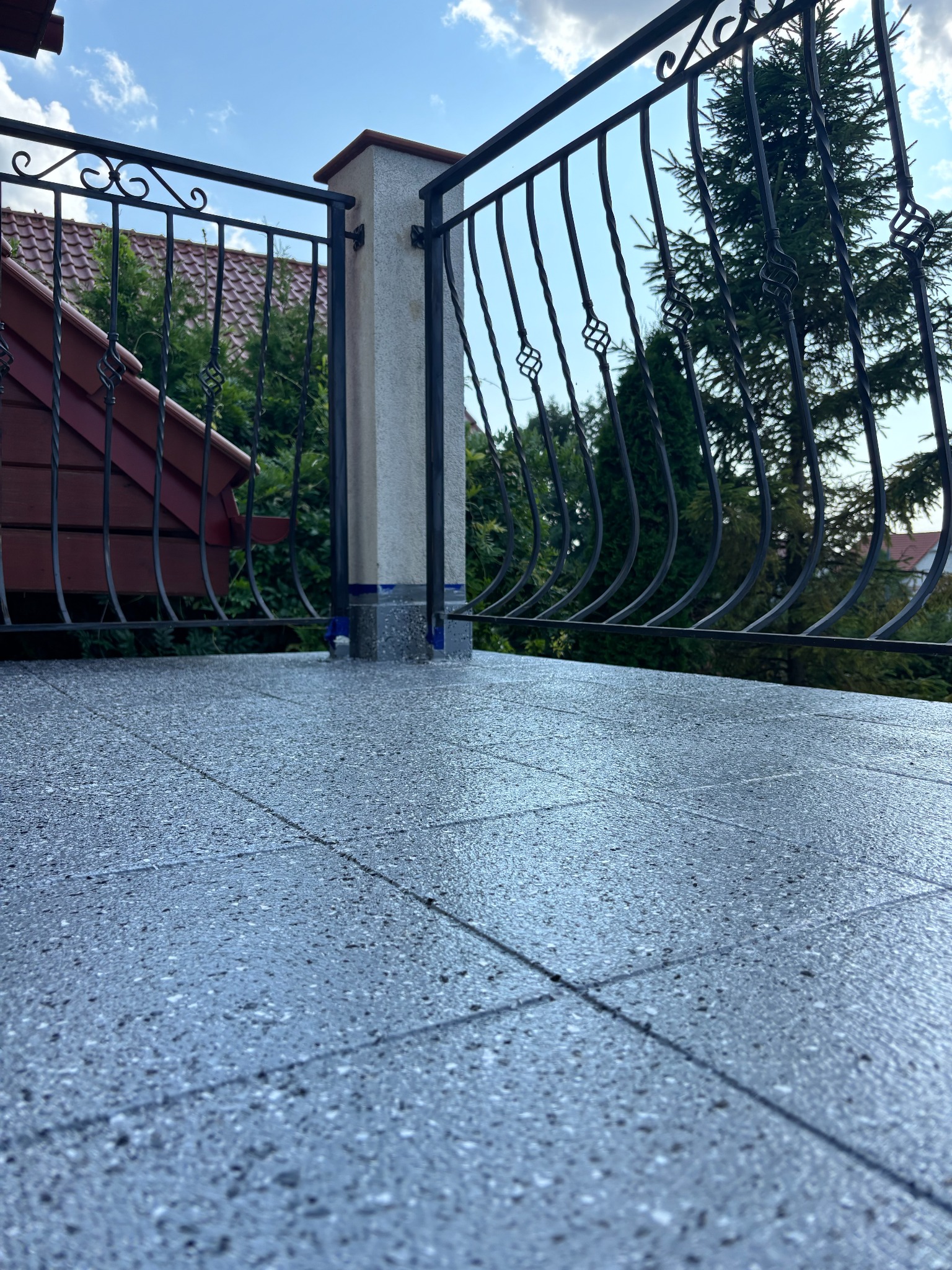 Szara, drobnoziarnista nawierzchnia balkonu z metalową balustradą i widokiem na zieleń. Teksturowana powierzchnia, nowoczesny design, solidne wykonanie.