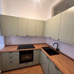 Oleksandr Urutskyi - Jasnozielona kuchnia z drewnianym blatem i czarną armaturą. Uwagę przykuwają frezowane fronty szafek i płytki ceramiczne na ścianie.