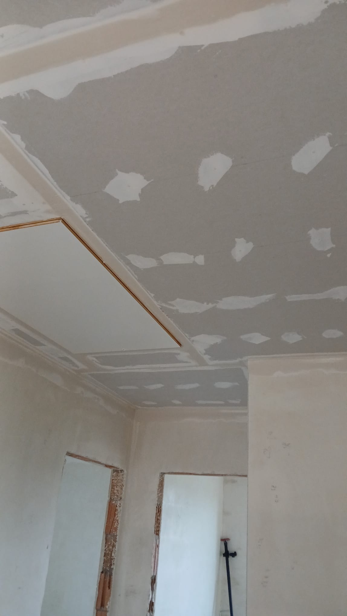 Sufit po szpachlowaniu z widocznymi łatami i fragmentem płyty gipsowej. Ściany w trakcie przygotowania do dalszych prac wykończeniowych. Wnętrze w stanie surowym.