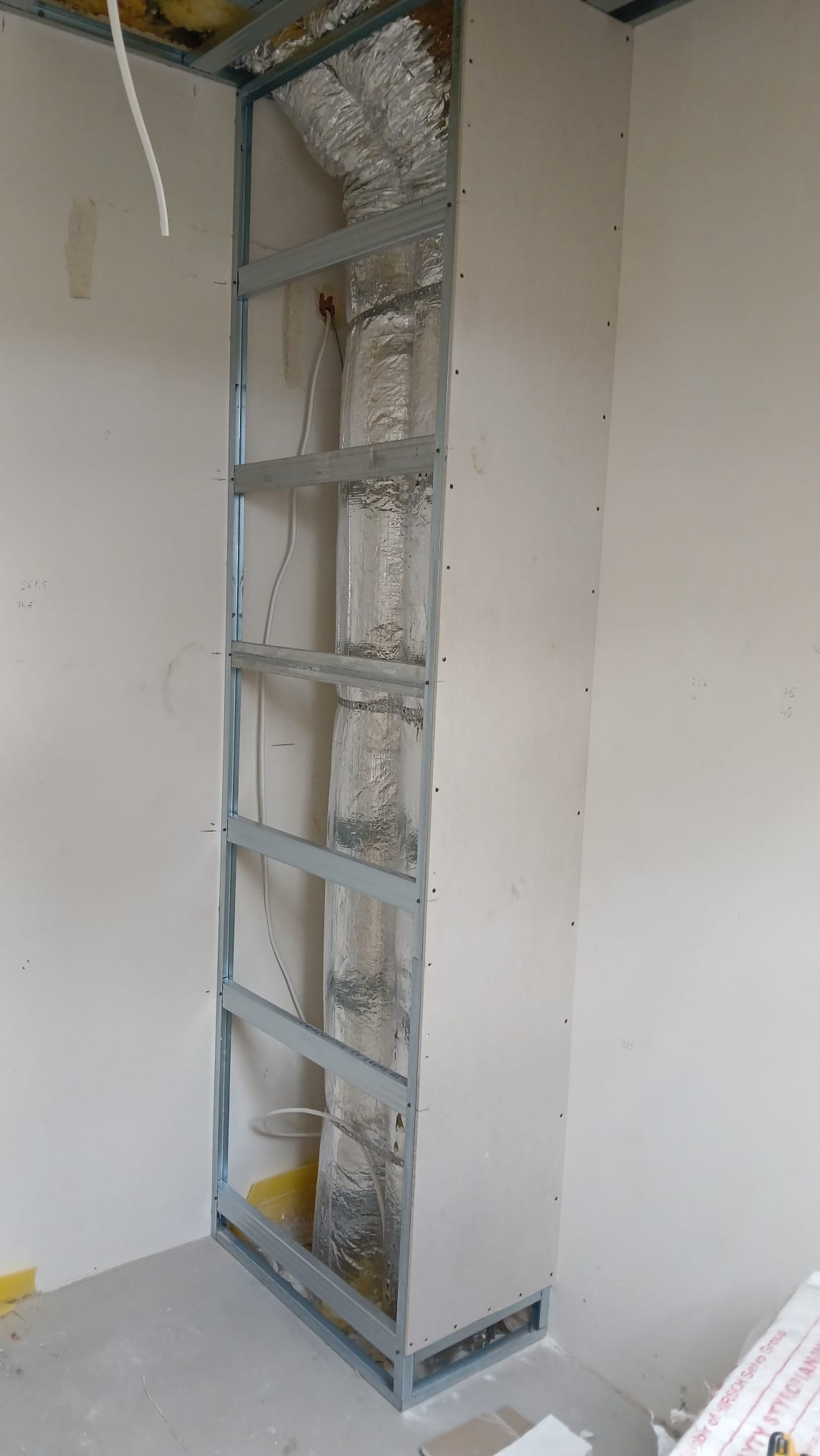 Konstrukcja z profili i płyty G-K, zabudowa instalacji wentylacyjnej w trakcie prac wykończeniowych. Widoczne przewody i izolacja. Ściany w surowym stanie.