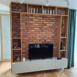 BAGO Meble - Szafka RTV z ceglaną ścianą i drewnianymi półkami w salonie. Dekoracyjne butelki na górnych półkach, parkiet w jodełkę. Nowoczesny design.