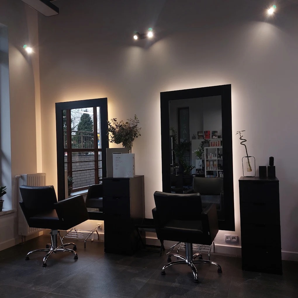 Nowoczesne wnętrze salonu z czarnymi fotelami fryzjerskimi, podświetlanymi lustrami i minimalistycznym wystrojem. Widok na ulicę przez okno.