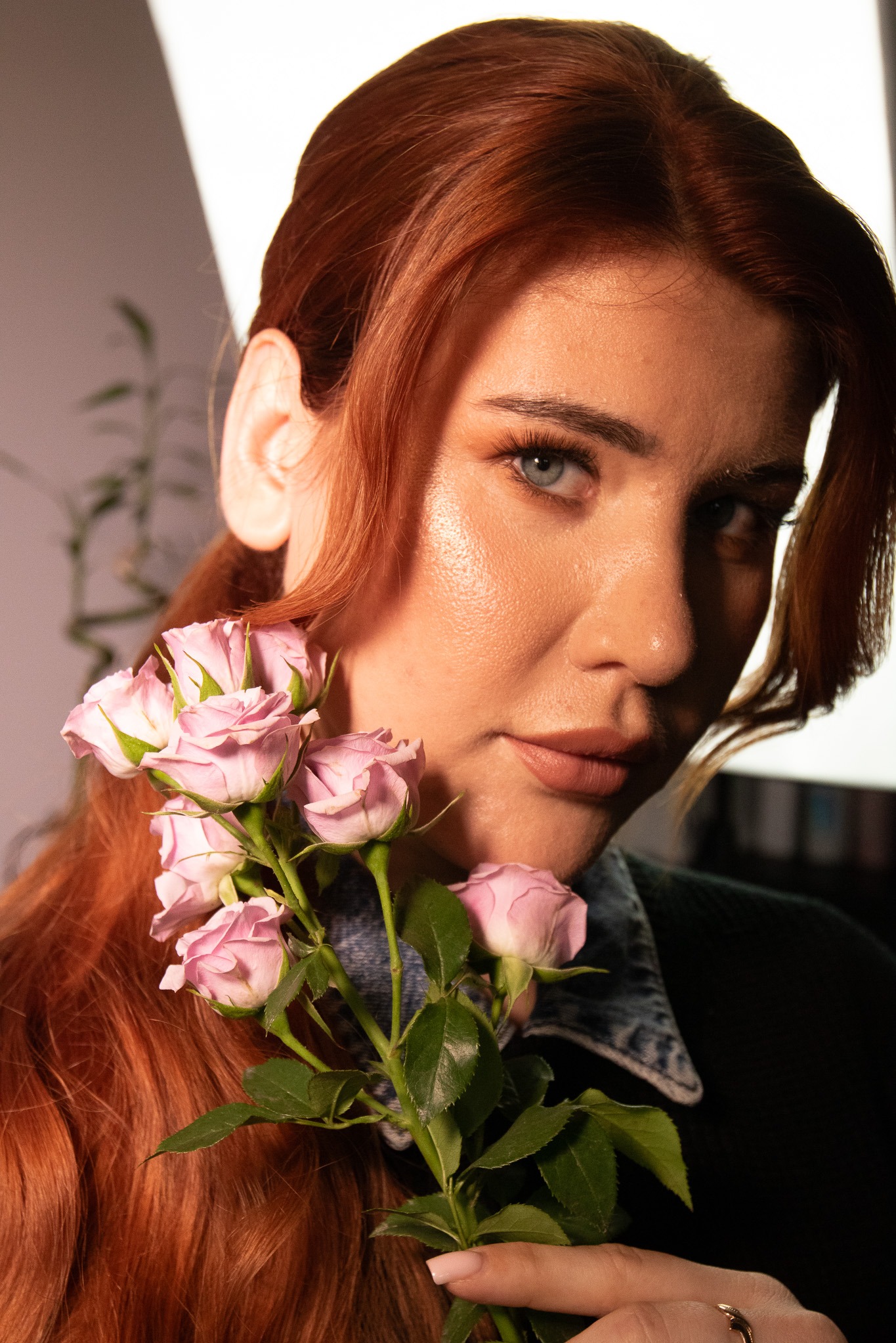 Portret kobiety z rudymi włosami, trzymającej bukiet różowych róż. Makijaż w odcieniach nude, niebieskie oczy. Subtelna fryzura z delikatnymi falami.