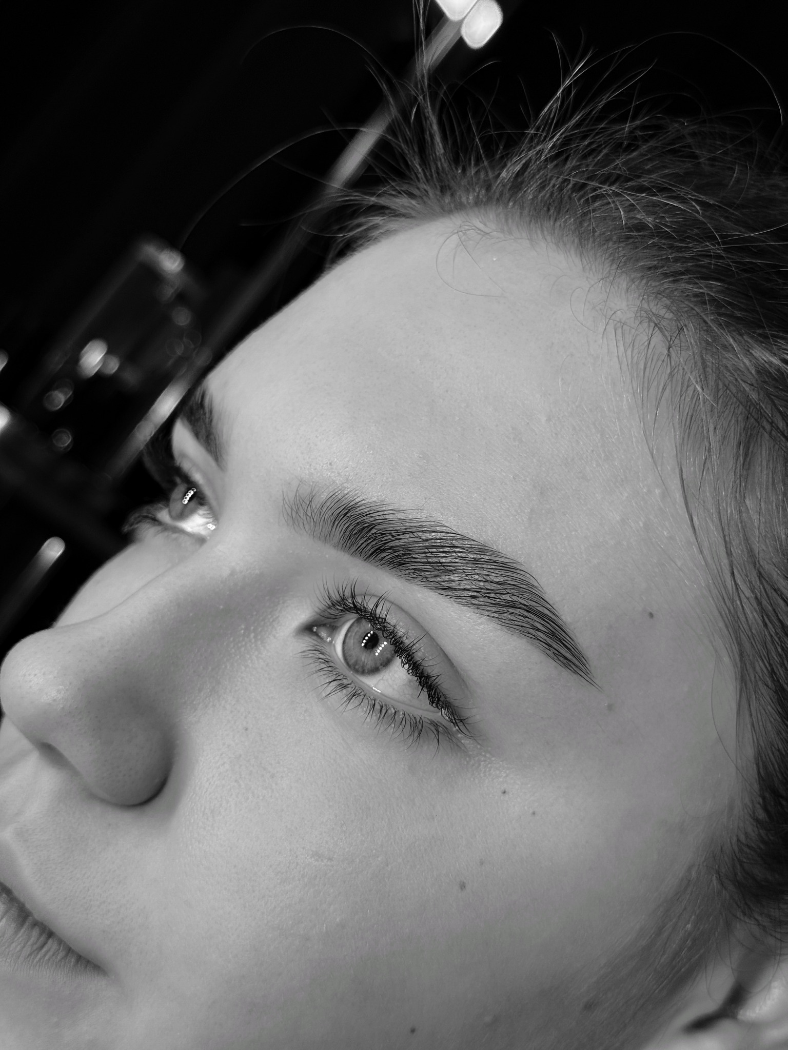 Zbliżenie na oko i idealnie ułożone brwi kobiety w czarno-białej tonacji, ukazujące precyzję zabiegu stylizacji brwi.