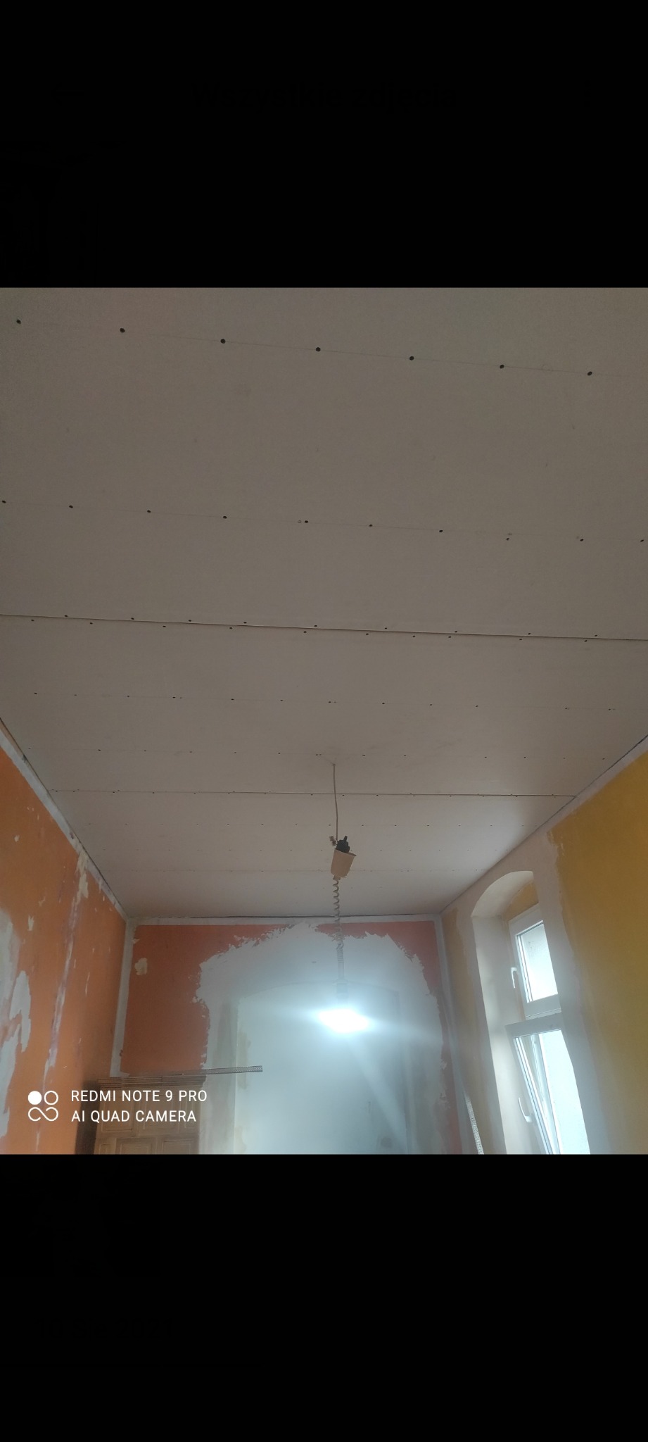 Sufit z płyt kartonowo-gipsowych w trakcie montażu, widoczne łączenia i wkręty. Ściany częściowo przygotowane do malowania, widoczne ślady szpachlowania.