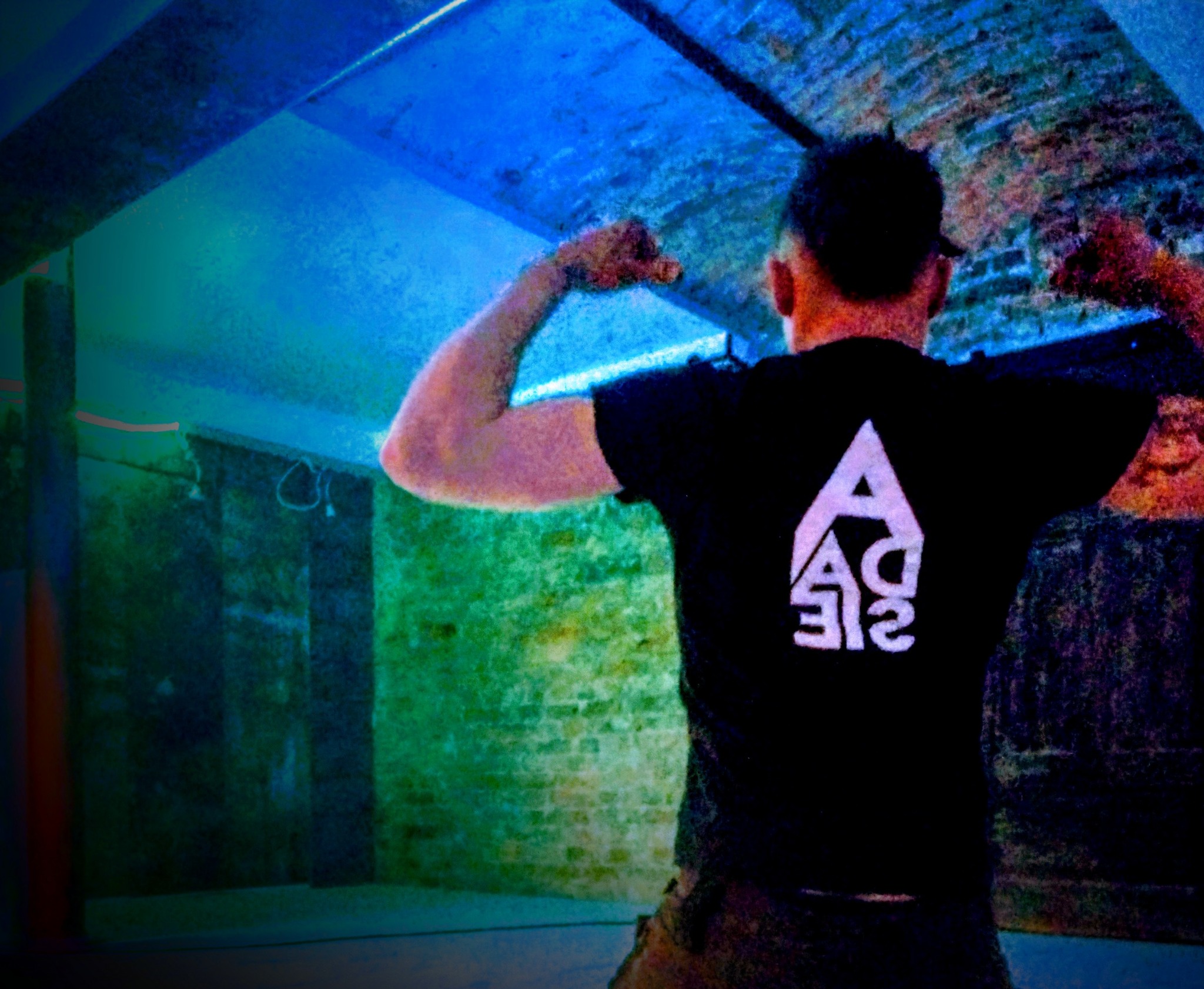 Mężczyzna tyłem prezentuje wyremontowane, surowe wnętrze z ceglanymi ścianami, oświetlone niebieskim światłem, z widocznym logo firmy na koszulce.