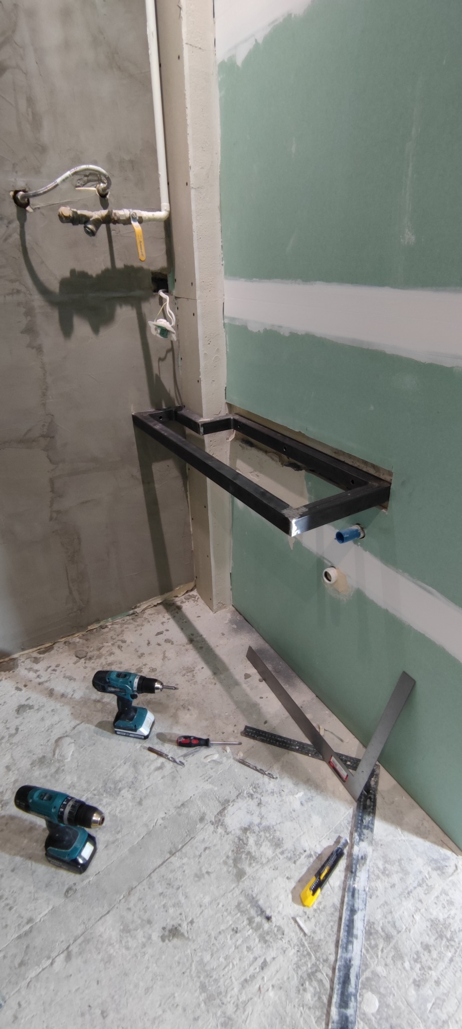 Montaż stelaża pod umywalkę w łazience, widoczne płyty karton-gips na ścianie, narzędzia budowlane na podłodze. W tle instalacja wodna i elektryczna.