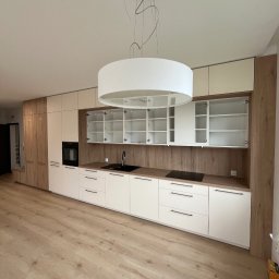 Prastora Dzianis Haponenka - Nowoczesna kuchnia na wymiar z białymi frontami i drewnianymi akcentami. Otwarta szafka z półkami, czarny zlew i płyta indukcyjna. Jasne drewno na podłodze.