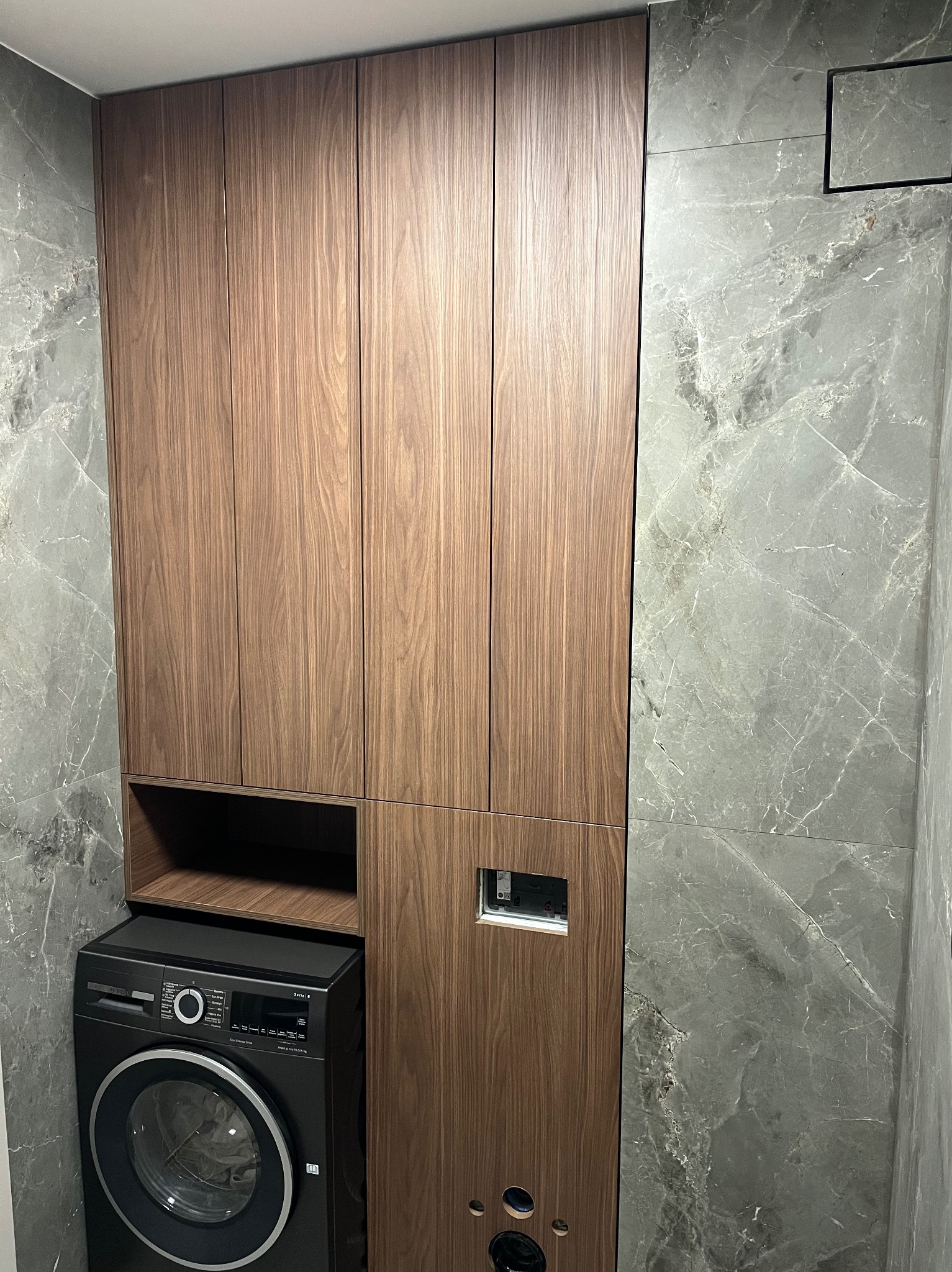 Drewniane szafki łazienkowe na wymiar, zintegrowane z pralką i szarą marmurową ścianą. Minimalistyczny design, nowoczesne wykończenie.