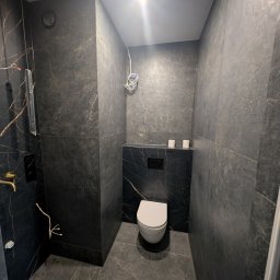 PORTO BAU OLEKSANDR ROMANETSKYI - Nowoczesna toaleta z czarnymi płytkami imitującymi marmur ze złotymi żyłami. Widoczne przyłącza elektryczne i hydrauliczne w trakcie montażu.