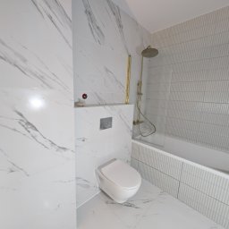 PORTO BAU OLEKSANDR ROMANETSKYI - Nowoczesna łazienka w bieli: marmurowe płytki, podwieszana toaleta i złota armatura prysznicowa. Minimalistyczny design z subtelnymi akcentami kolorystycznymi.