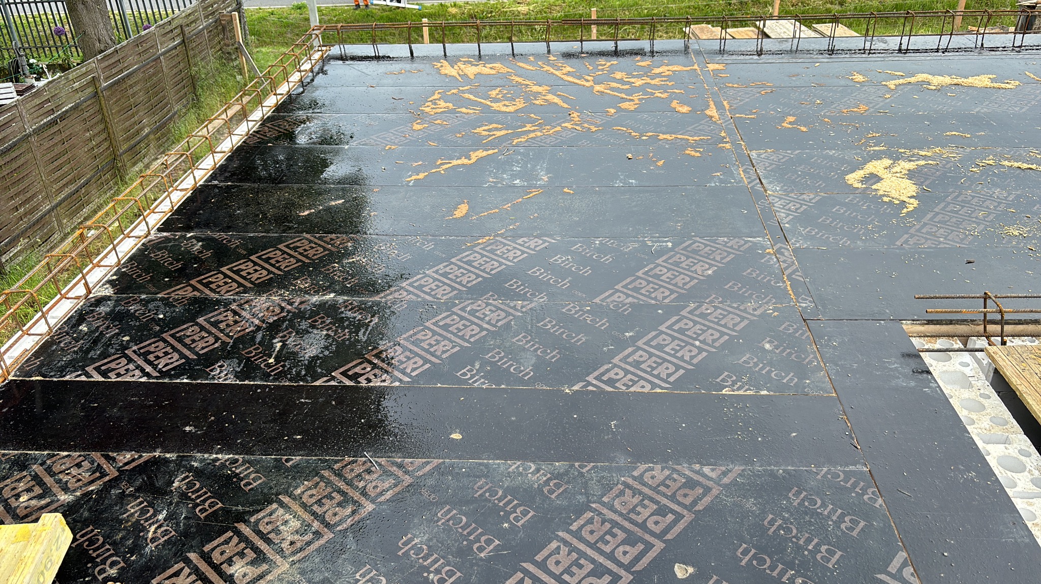 Szczegółowy widok szalunku stropowego z widocznym zbrojeniem i deskami szalunkowymi z nadrukiem, przygotowanego do zalewania betonem. Widoczne ślady po betonie.