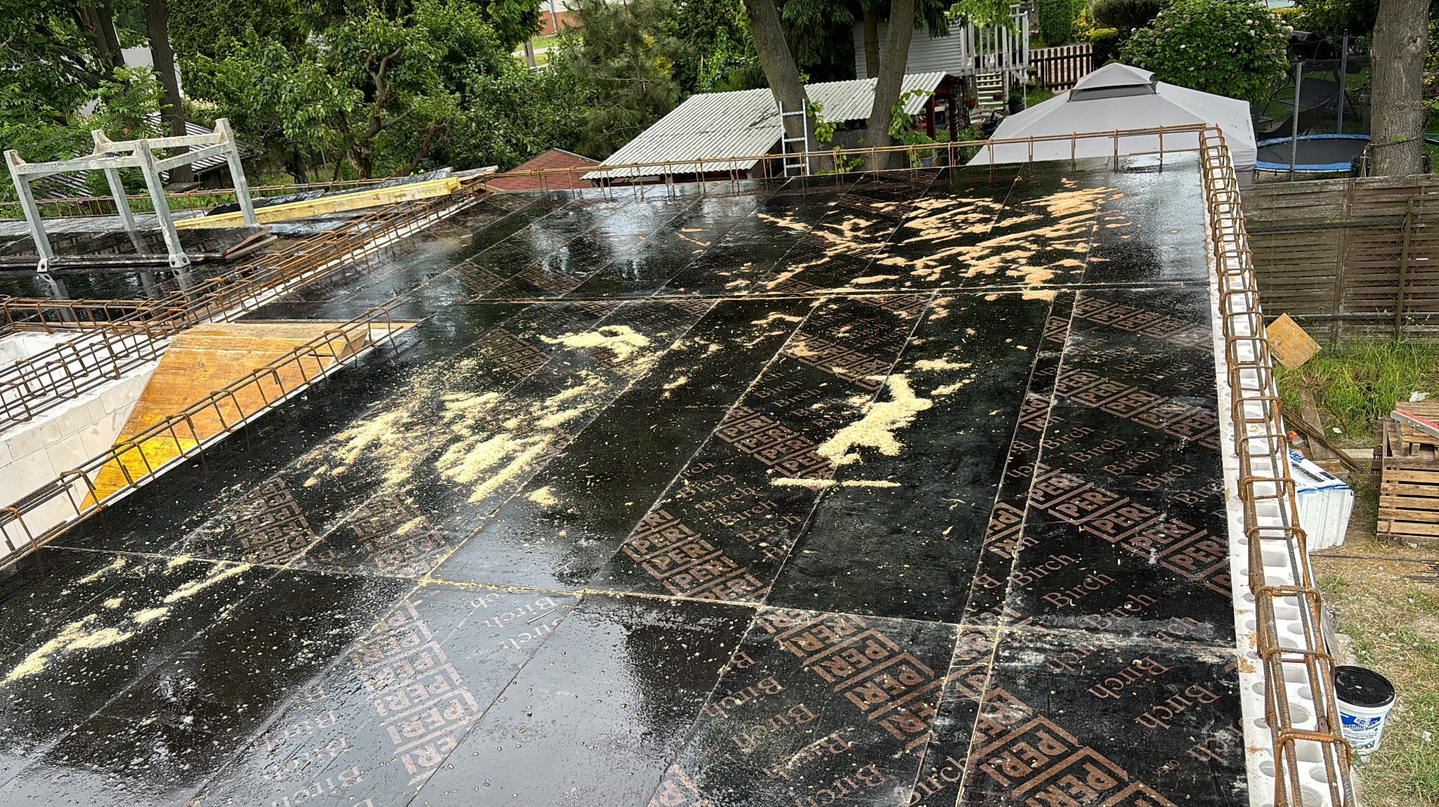 Zalane wodą płyty szalunkowe PERI Birch na stropie budynku w trakcie budowy, z widocznym zbrojeniem i elementami konstrukcyjnymi. Widok z góry na plac budowy.