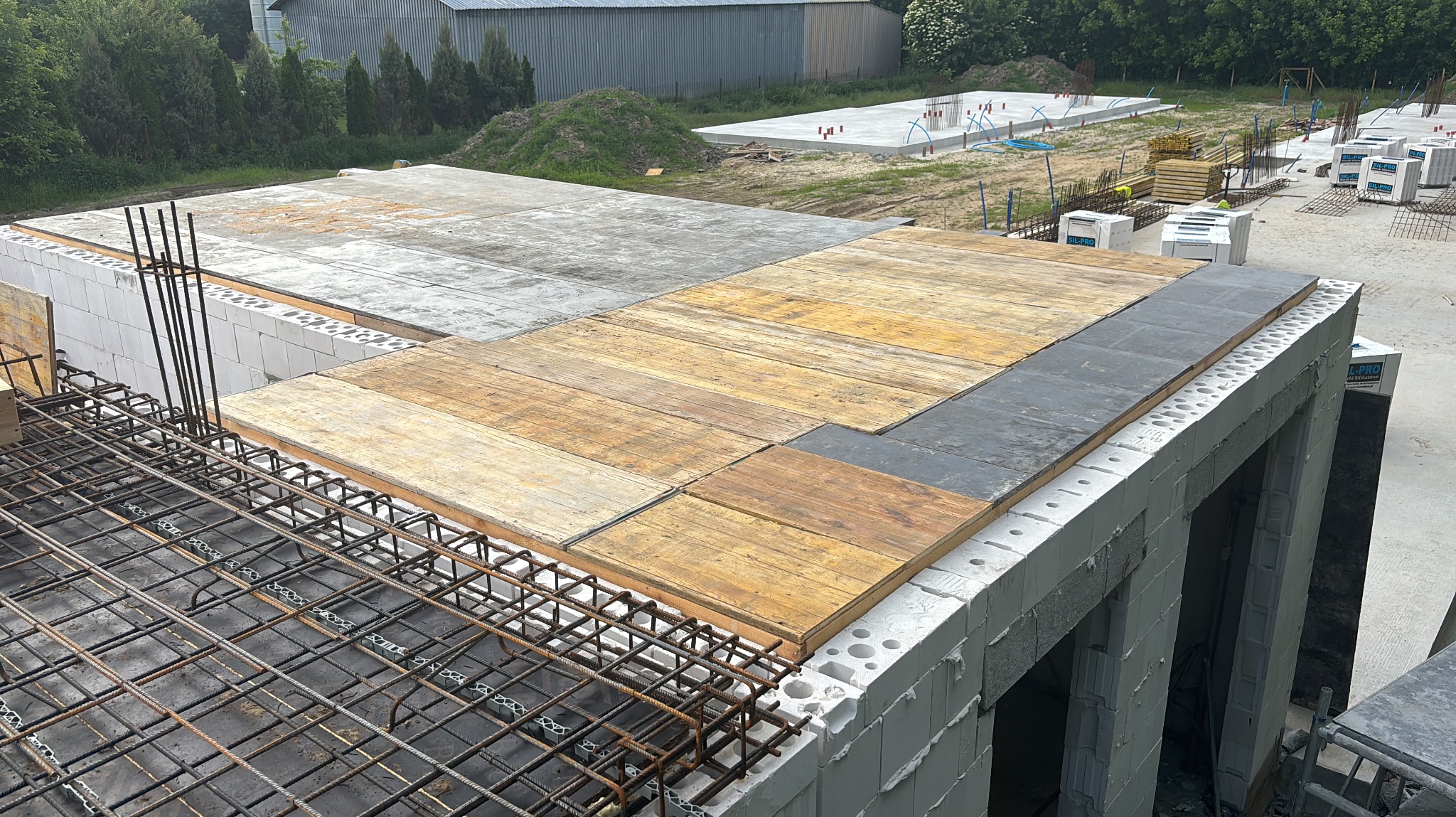 Budowa domu: ściany z betonu komórkowego, szalunek stropu z desek i płyty, zbrojenie. W tle fundamenty kolejnego budynku.