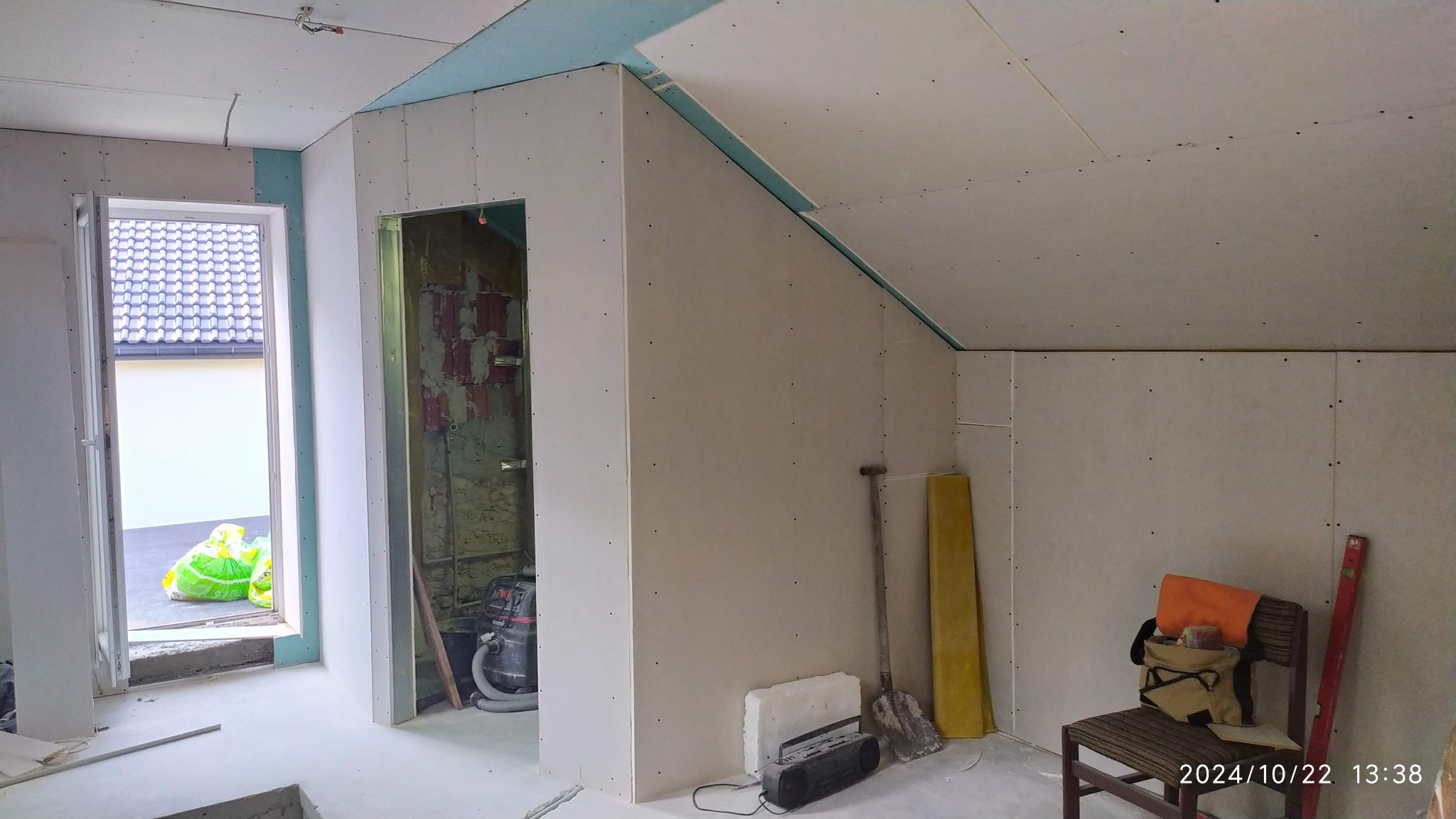 Montaż płyt G-K na poddaszu w Wojkowicach Kościelnych. Widoczne narzędzia, szpachla, oraz fragment okna. Ściany przygotowane do dalszych prac wykończeniowych.