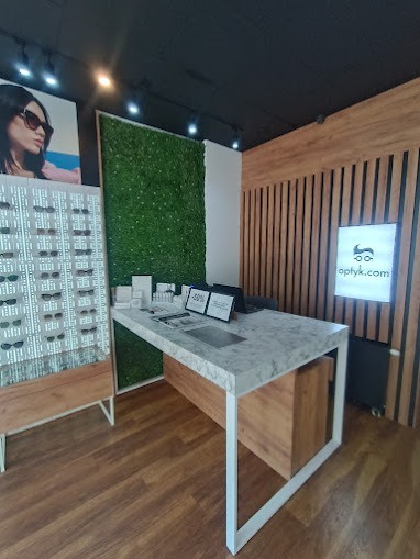 Nowoczesny salon optyczny: ekspozycja okularów, lada z marmurowym blatem, zielona ściana. Minimalistyczny design, jasne oświetlenie, eleganckie wykończenie.