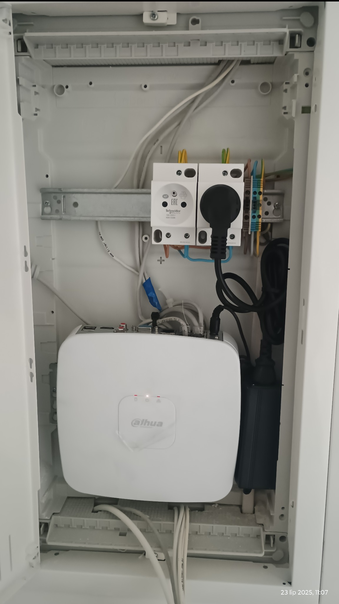 Szafka z białym rejestratorem Dahua, gniazdkami Schneider i okablowaniem. Widoczne złącza i przewody. Instalacja wewnątrz obudowy.