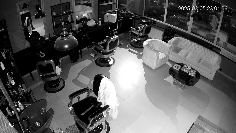 Czarno-biały obraz z kamery monitoringu przedstawia wnętrze eleganckiego salonu fryzjerskiego z fotelami, kanapami i stanowiskami pracy. Widoczny datownik w prawym górnym rogu.