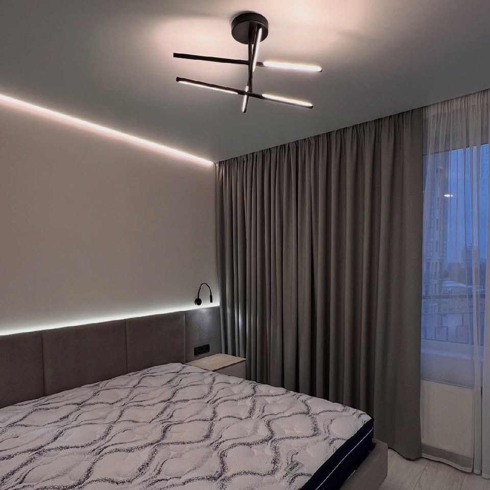 Nowoczesna sypialnia z łóżkiem, zasłonami i designerską lampą sufitową. Oświetlenie LED podkreśla minimalistyczny charakter wnętrza.