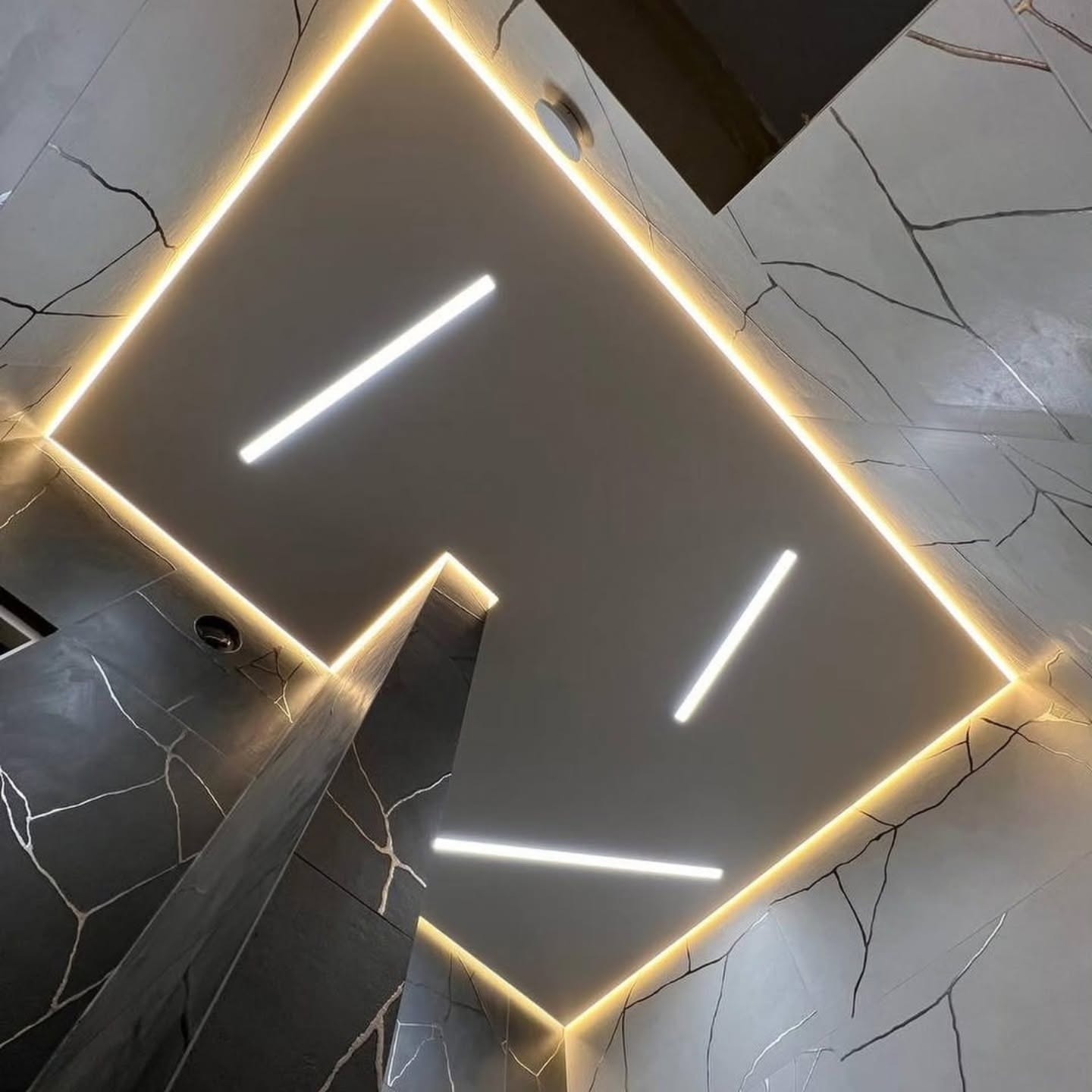 Nowoczesna łazienka z podświetlanym sufitem i ścianami w marmurkowe wzory. Minimalistyczne oświetlenie liniowe. Nietypowy kadr z dołu podkreśla design.