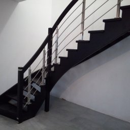 Błażej Owczarek - Ciemne schody z metalową balustradą w nowoczesnym wnętrzu. Minimalistyczny design, proste linie, szare ściany i podłoga. Ujęcie z dołu, podkreślające geometrię konstrukcji.