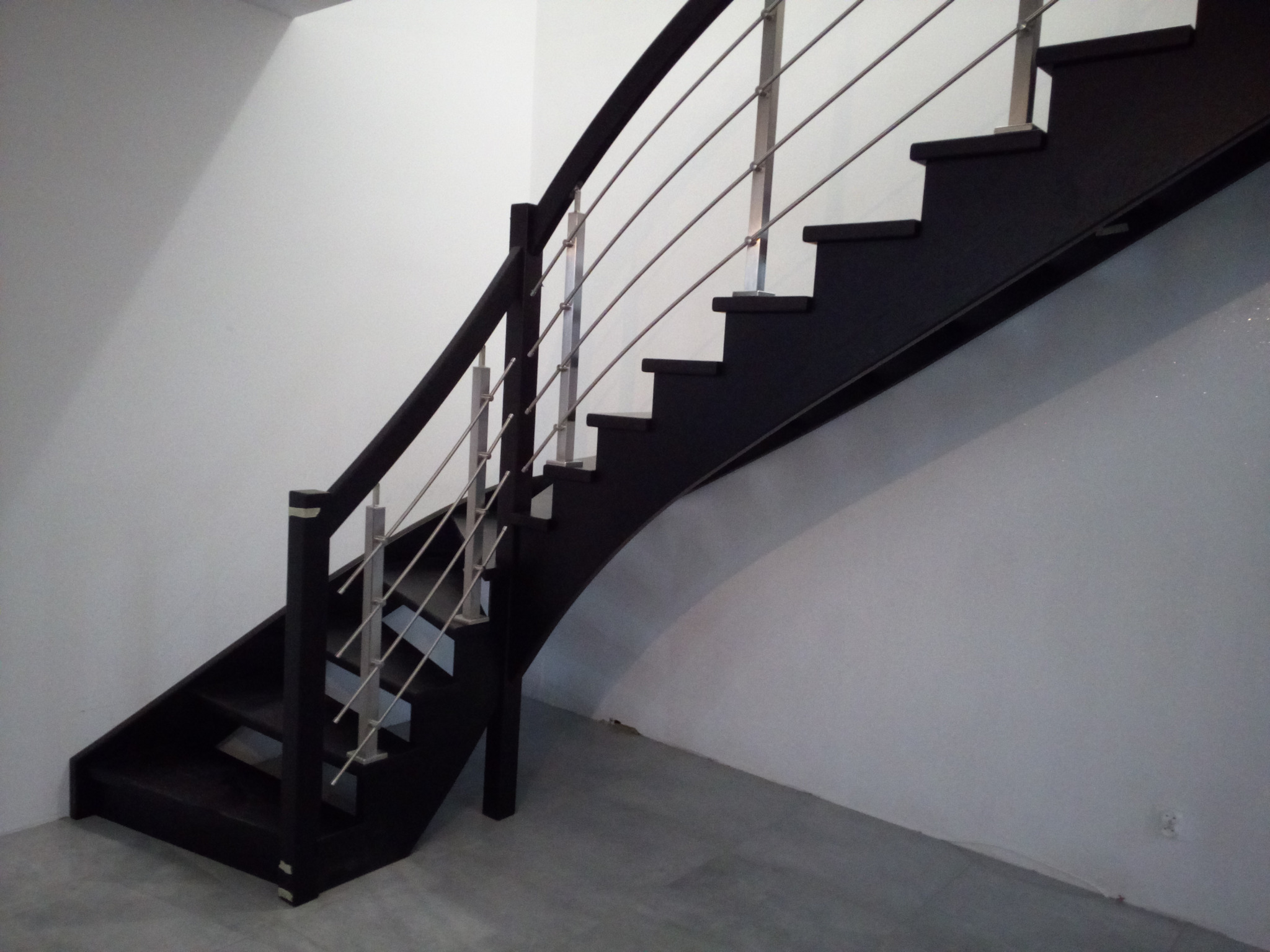 Ciemne schody z metalową balustradą w nowoczesnym wnętrzu. Minimalistyczny design, proste linie, szare ściany i podłoga. Ujęcie z dołu, podkreślające geometrię konstrukcji.