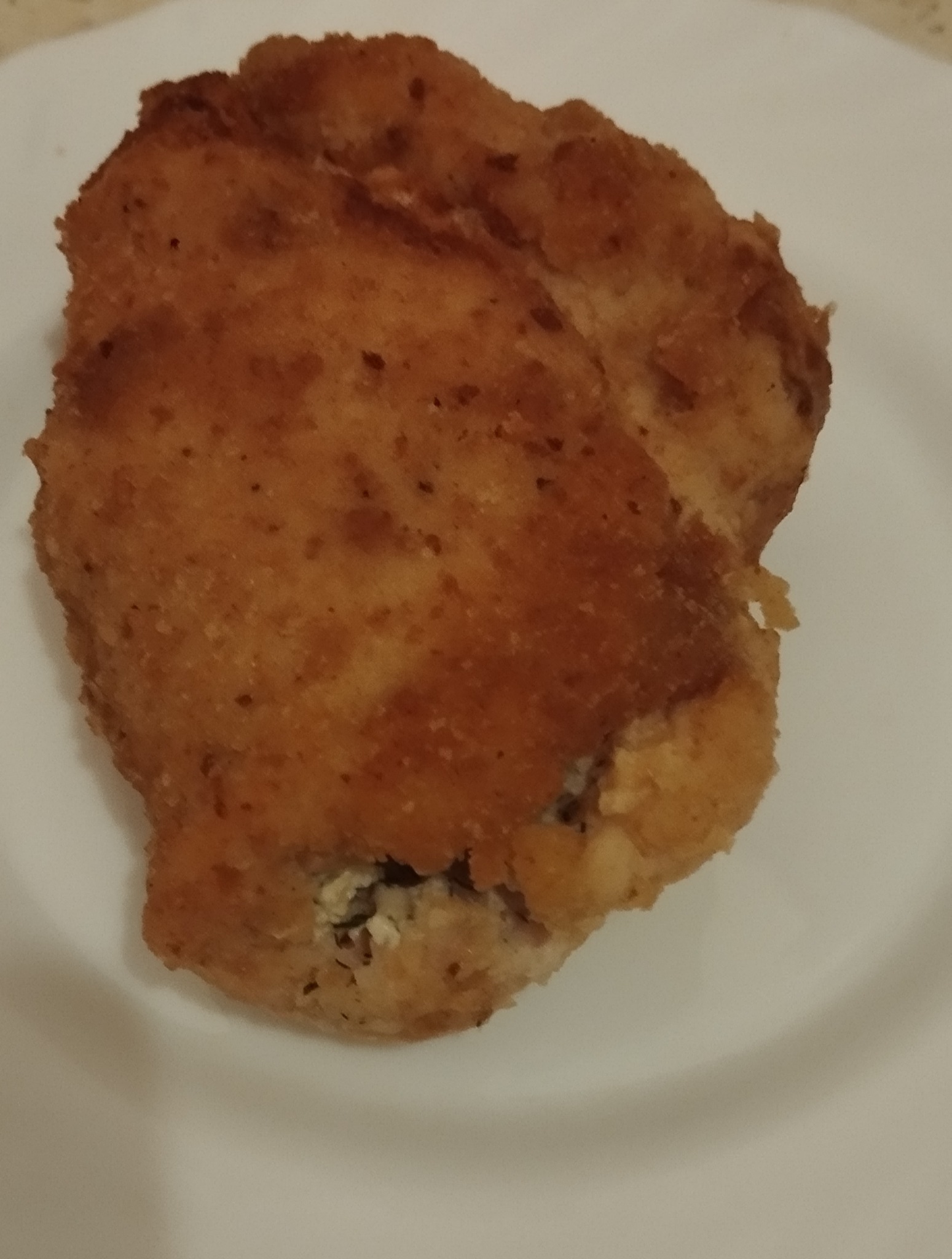 Pojedynczy, panierowany kotlet na białym talerzu, sfotografowany z bliska. Widoczne detale panierki i farszu. Idealny przykład dania z cateringu.