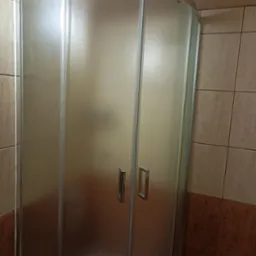 Kabina prysznicowa z matowego szkła w narożniku łazienki, widoczne chromowane uchwyty i płytki w odcieniach beżu i brązu. Widok na zamontowaną kabinę.