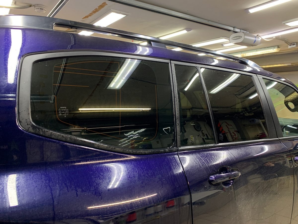 Częściowy widok boku ciemnoniebieskiego SUV-a z przyciemnionymi szybami w warsztacie, z widocznymi śladami wody po myciu. Detal na tylnych szybach.