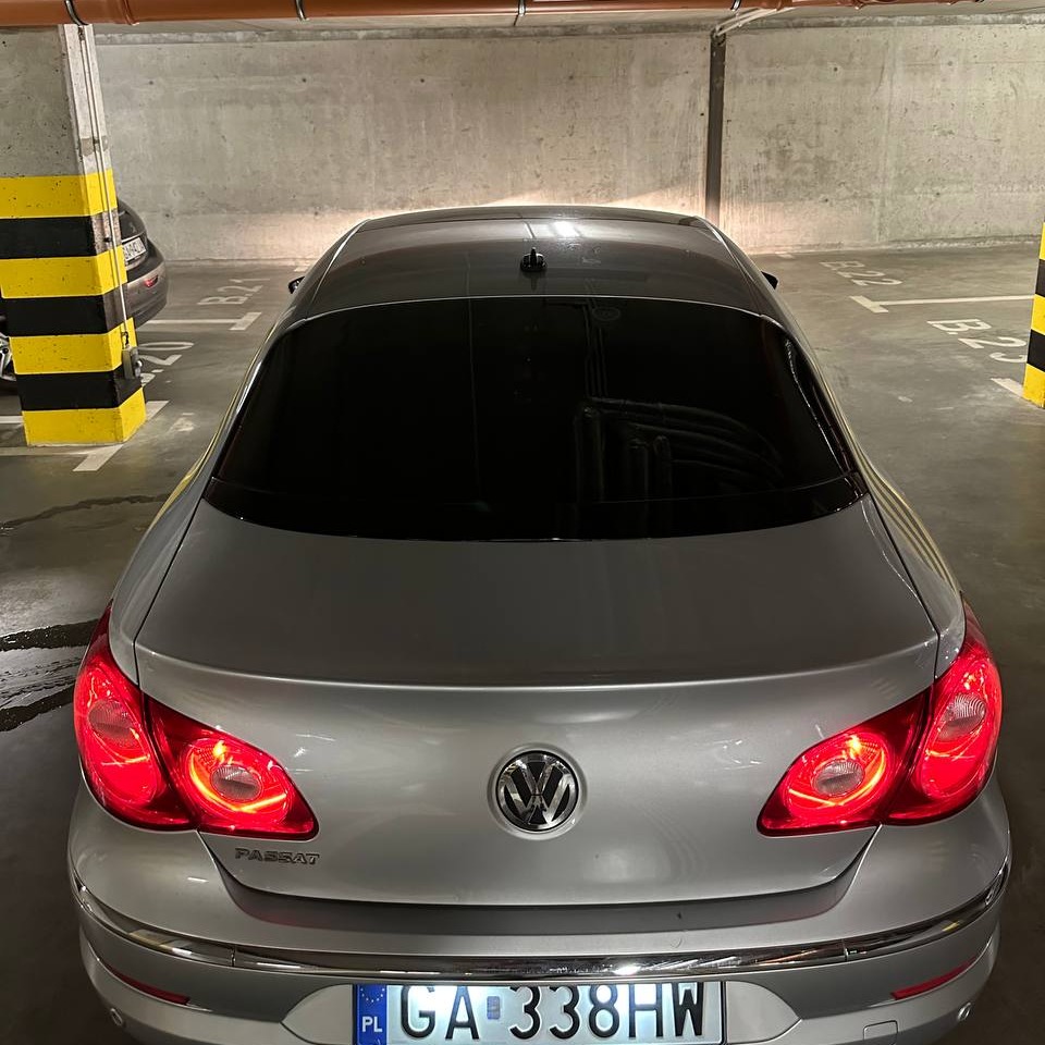 Srebrny Volkswagen Passat CC z przyciemnionymi szybami, zaparkowany w garażu podziemnym, widok z tyłu, światła stopu włączone, tablica rejestracyjna widoczna.