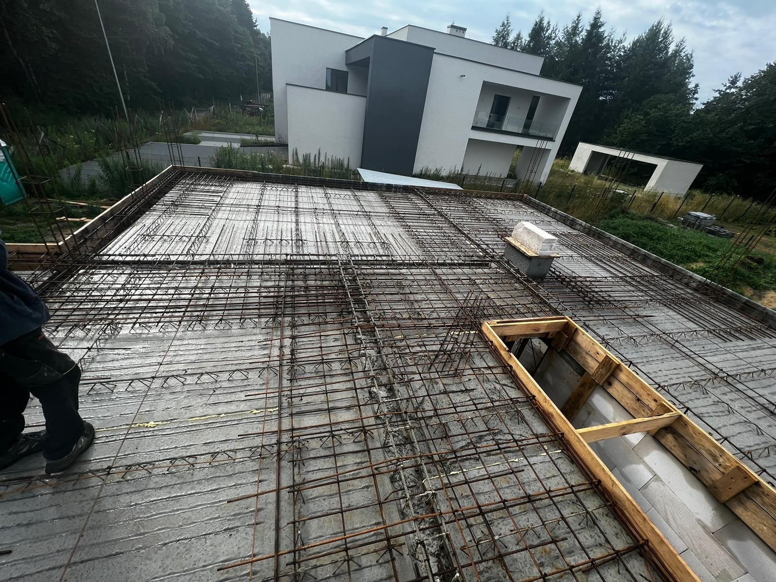 Zbrojenie stropu budynku jednorodzinnego w Jaworznie, przygotowane do zalania betonem. Widoczne stalowe pręty i szalunki okienne. W tle nowoczesny dom.