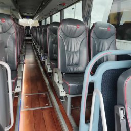 SIGMA PODRÓŻE - Wnętrze luksusowego autobusu z rzędem skórzanych foteli Ötztaler z czerwonymi akcentami i drewnianą podłogą, oświetlonego subtelnym światłem.