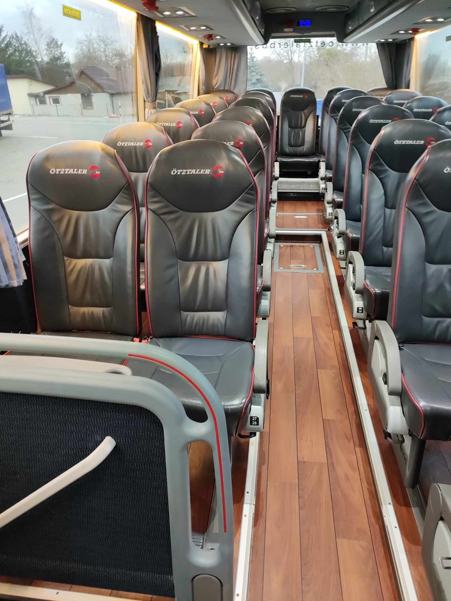 Wnętrze luksusowego autokaru z drewnianą podłogą i skórzanymi fotelami z logo Ötztaler, widok na puste siedzenia i przejście.