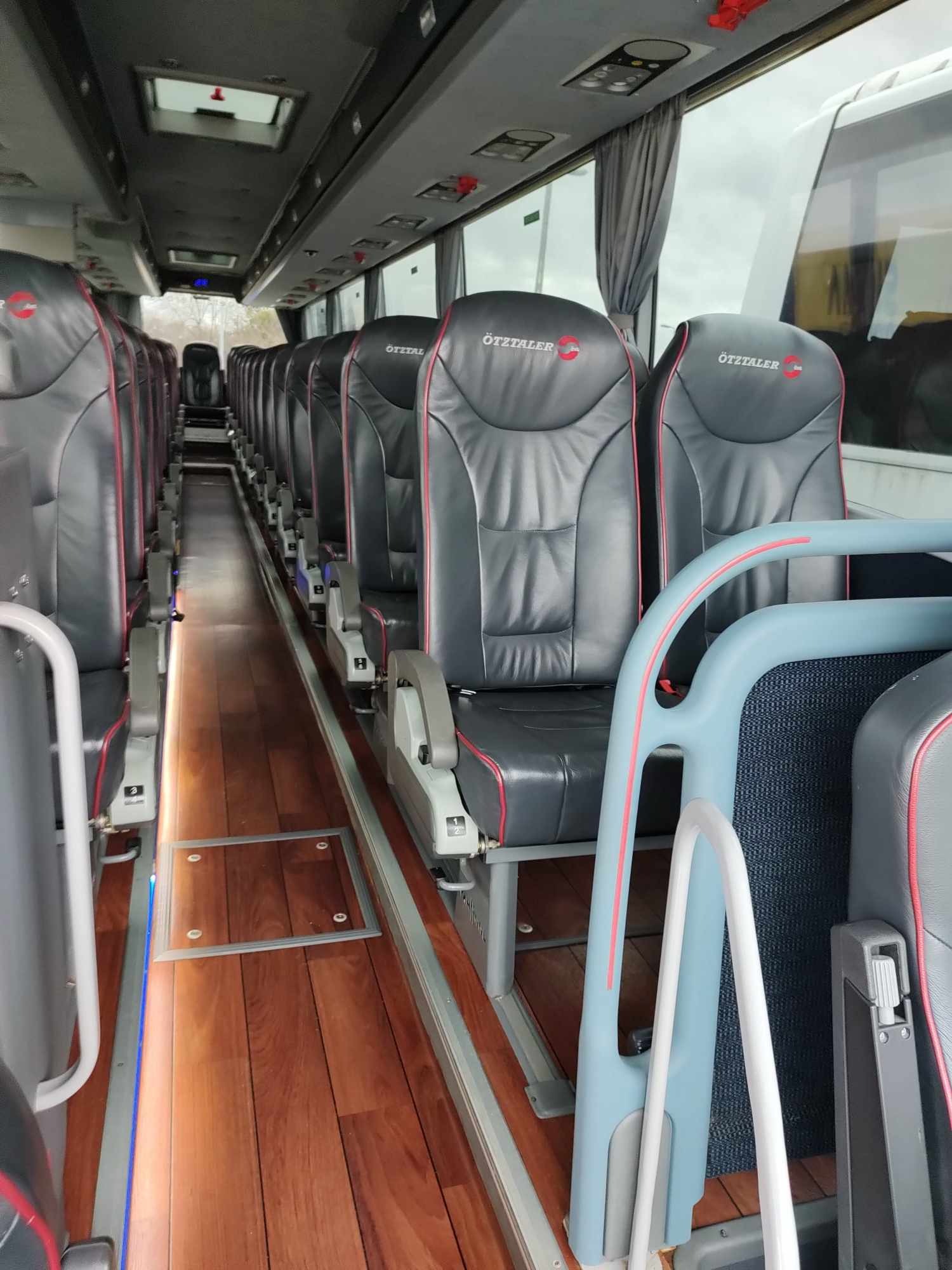 Wnętrze luksusowego autobusu z rzędem skórzanych foteli Ötztaler z czerwonymi akcentami i drewnianą podłogą, oświetlonego subtelnym światłem.
