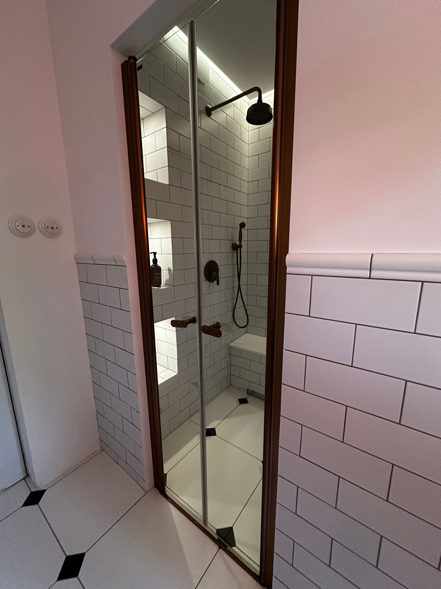 Nowoczesna kabina prysznicowa z brązowymi ramami i białymi płytkami w stylu retro, z wnęką na kosmetyki i siedziskiem. Eleganckie wykończenie łazienki.